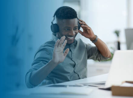 Person wearing headphones and waving hello during a virtual meeting.